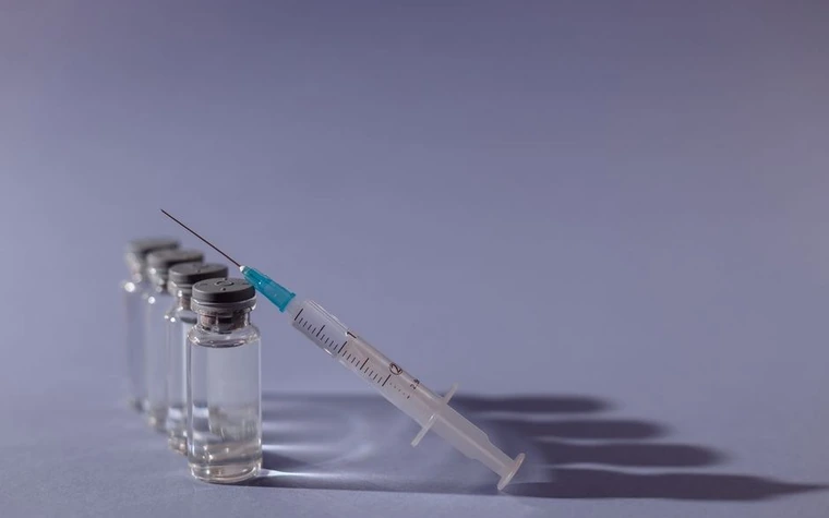 A syringe and vaccine vials arranged on a gray surface