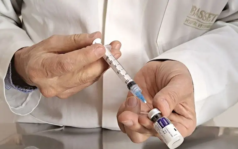 A veterinarian preparing a syringe and vaccine vial on a stainless steel table