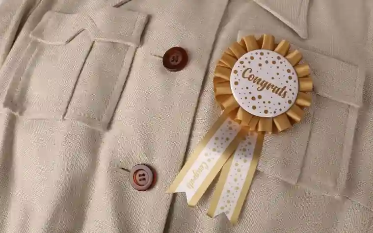 A gold Congrats award rosette with ribbons pinned on a beige jacket