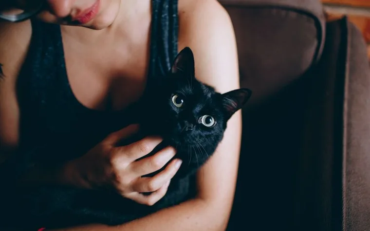 A woman holding a black cat close indoors