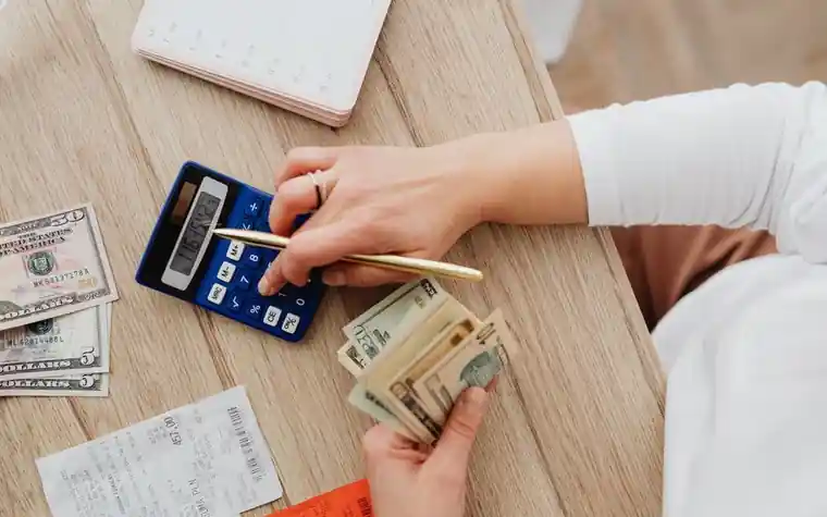 A person calculating pet costs with a calculator and cash on a table