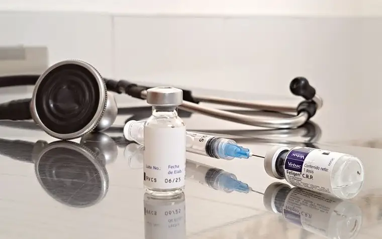Vaccine vials and a syringe with a stethoscope on a reflective clinic table
