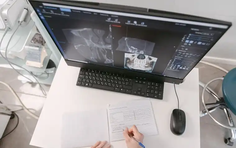 A hand writing notes beside X-ray images on a monitor