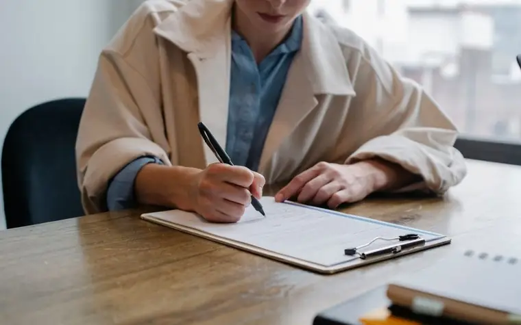 Person filling out a registration form on a clipboard at a wooden desk