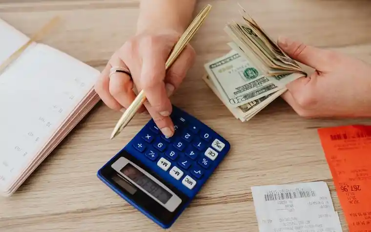 Hands using a calculator beside cash and receipts on a desk
