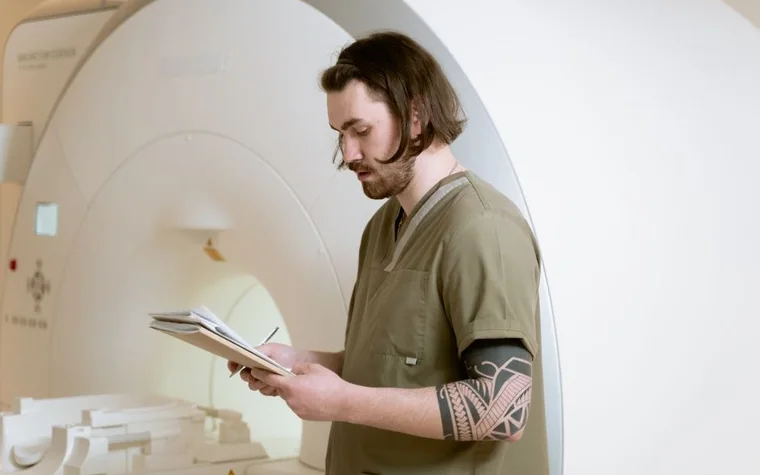 A technician reading notes beside an MRI scanner in a hospital imaging room