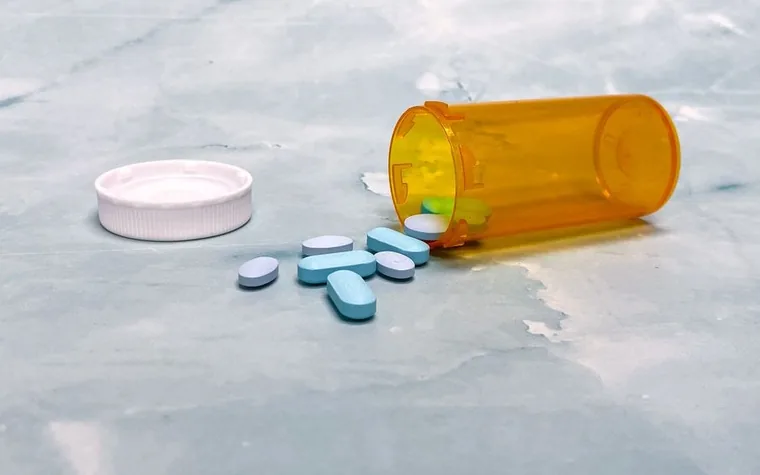 A prescription bottle with pills spilled on a gray surface