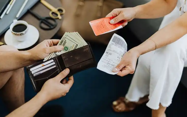 A person holding cash and a receipt over a wallet