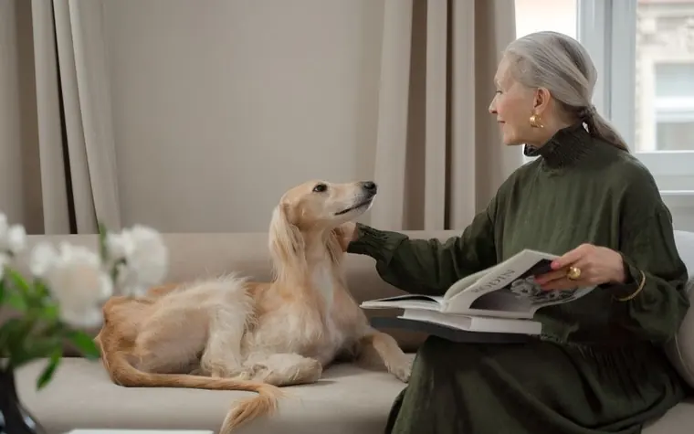 A woman reading paperwork with her dog on the couch