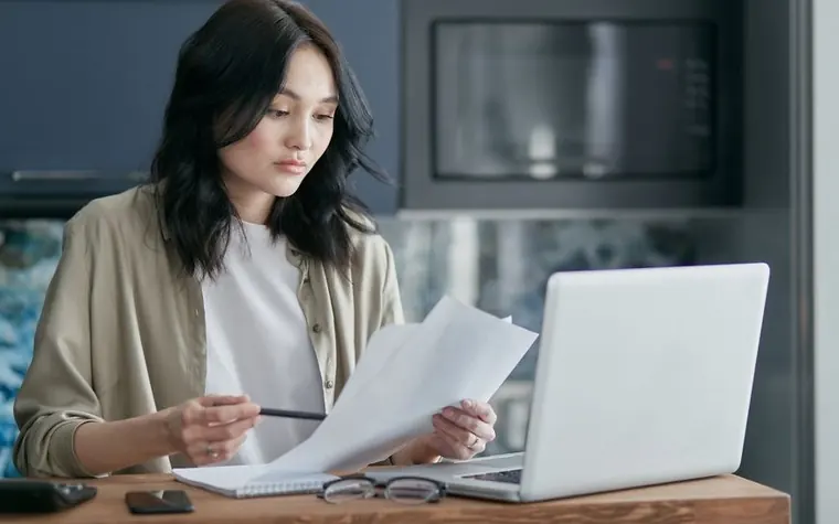 A woman reviewing documents and a laptop at a desk