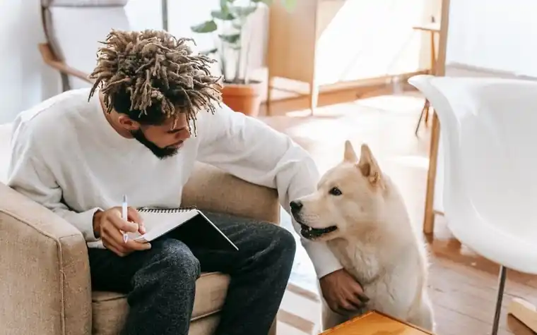 A man sitting in an armchair with a notepad, his dog beside him
