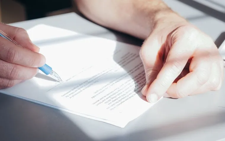 Close-up of a hand signing an insurance enrollment document with a pen