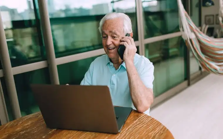 Elderly man on a phone call while using a laptop at home