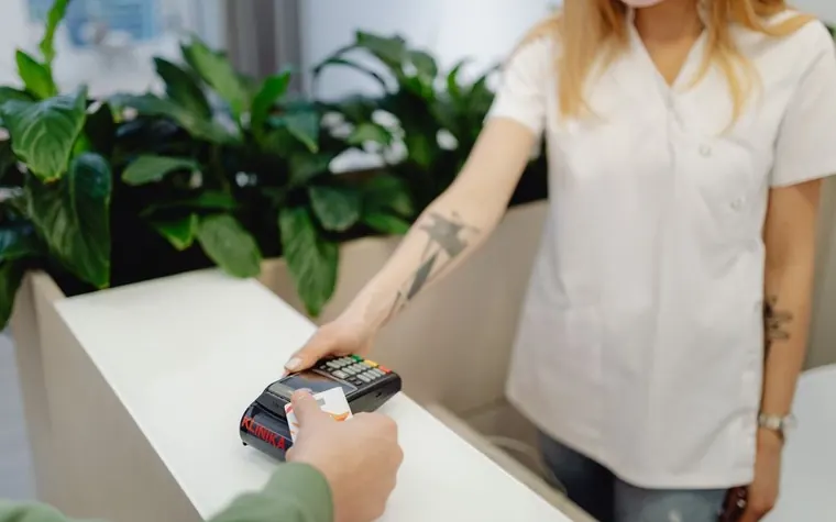 Clinic staff member holding a card reader while a customer taps a card to pay at a reception desk
