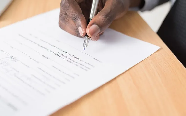 Hand holding a fountain pen signing a document on a wooden desk