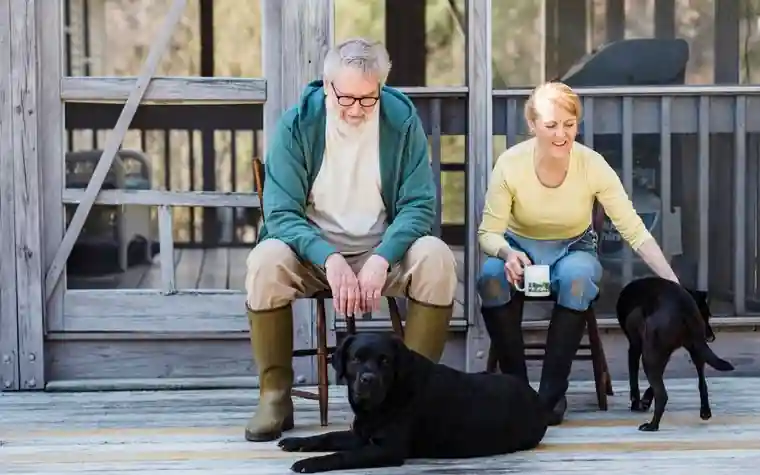 Older couple sitting on a wooden porch with two black dogs resting at their feet