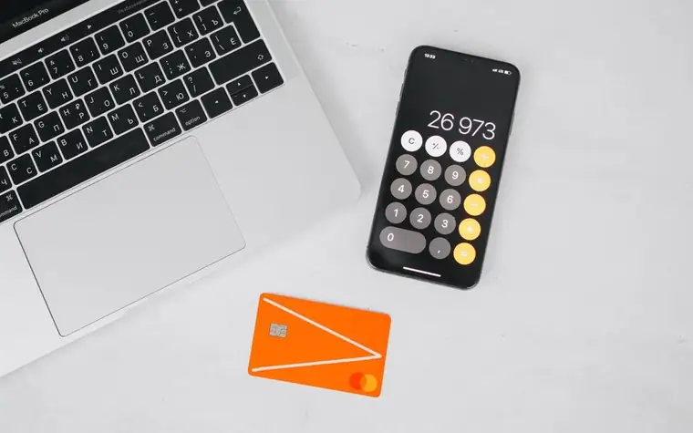 Smartphone calculator beside a laptop and an orange card on a white desk