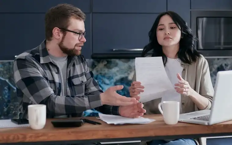 Couple at a kitchen table reviewing paperwork and a laptop together