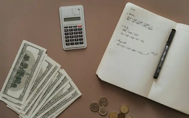 Calculator, notebook, pen and US dollar bills on a desk