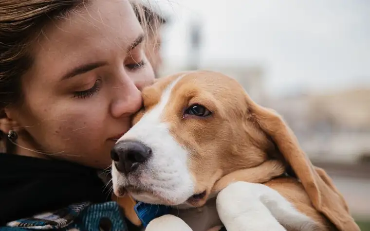 A woman hugging a beagle outdoors with her eyes closed