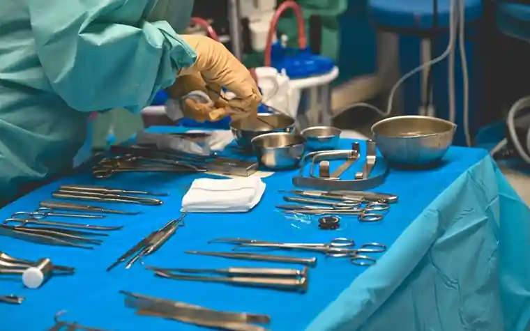 A surgeon's gloved hands arranging sterile instruments on a blue surgical table