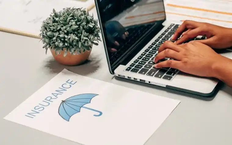 A laptop on a desk beside a printed insurance sheet with an umbrella logo