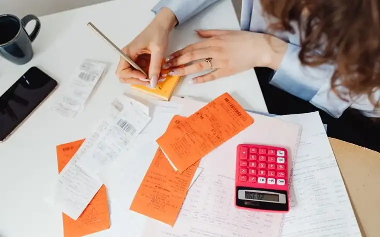 Receipts and a calculator spread across a desk with a hand writing