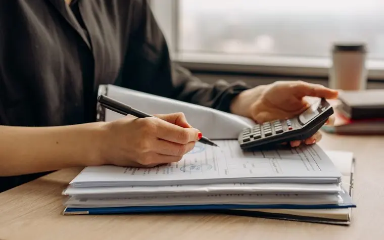 A person reviewing paperwork with a calculator at a desk