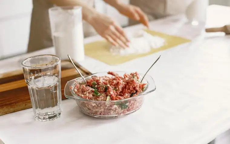 Raw ground meat and ingredients laid out in a glass bowl on a kitchen counter