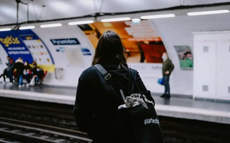 A woman on a subway platform wearing a backpack with a cat inside