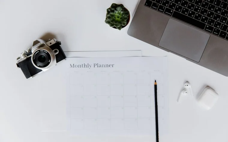 A monthly planner calendar on a white desk next to a laptop and pencil