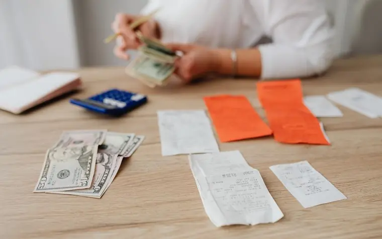 Hands sorting receipts, cash and a calculator on a wooden table