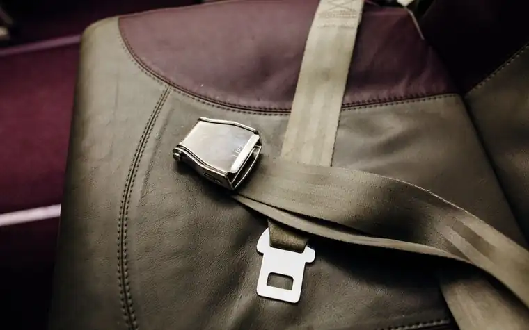 A leather airplane seat belt strap and metal buckle on a seat
