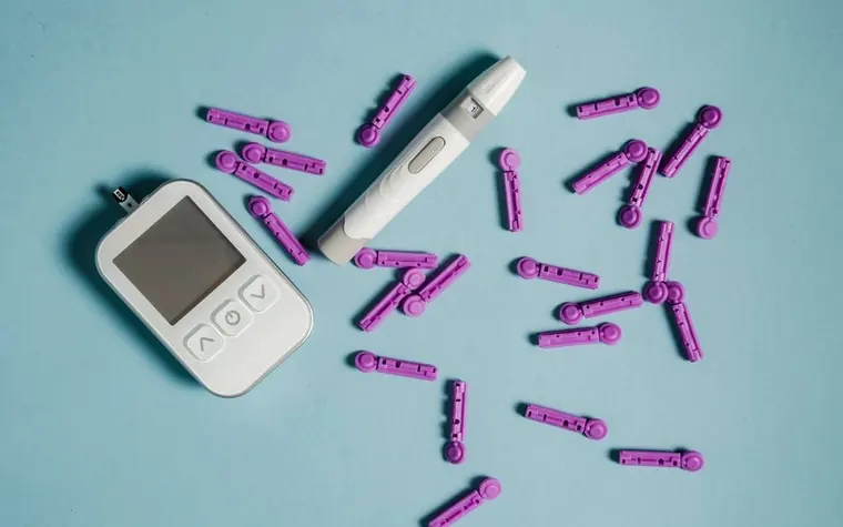 A glucose meter and test strips on a table next to insulin supplies