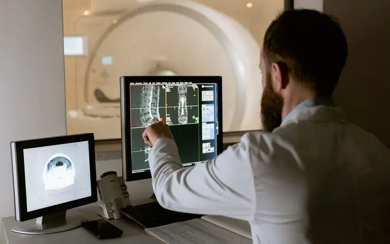 A person reviewing diagnostic scan images on a monitor with an MRI machine in the background