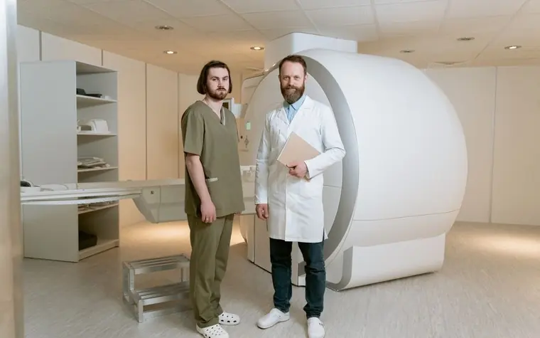 Two medical staff standing beside a large MRI scanner in an imaging room