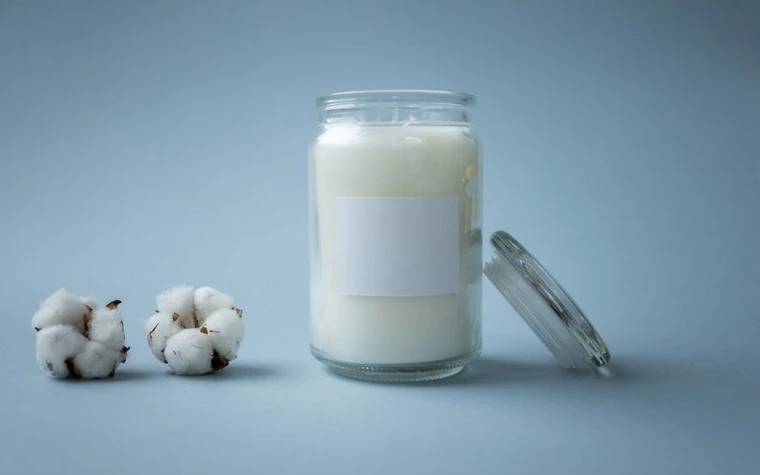 A minimalist glass jar candle beside soft cotton balls on a plain background
