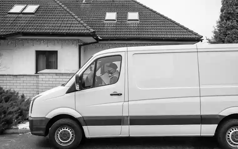 Black and white photo of a plain white cargo van parked outside a house