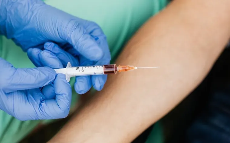Close-up of a gloved hand holding a syringe during a blood draw