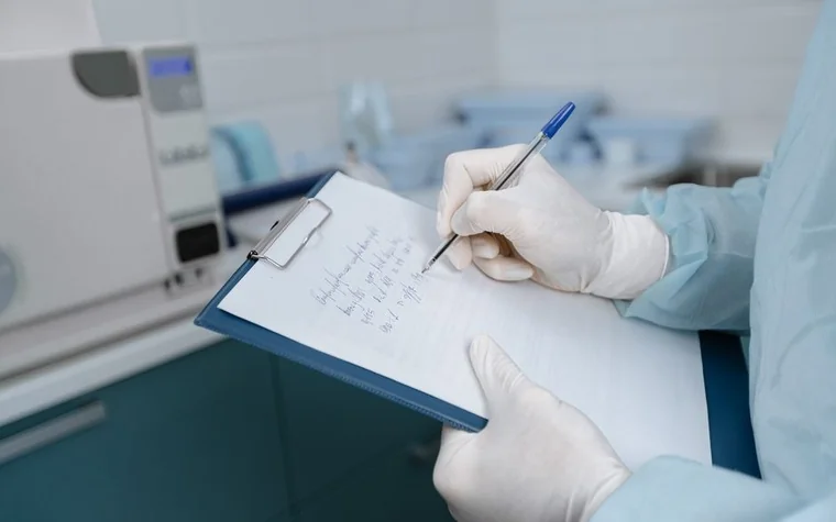 Gloved hand writing notes on a clipboard in a clinic setting