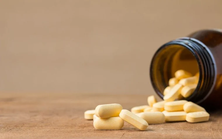 Yellow tablets spilling out of an open pill bottle on a wood table