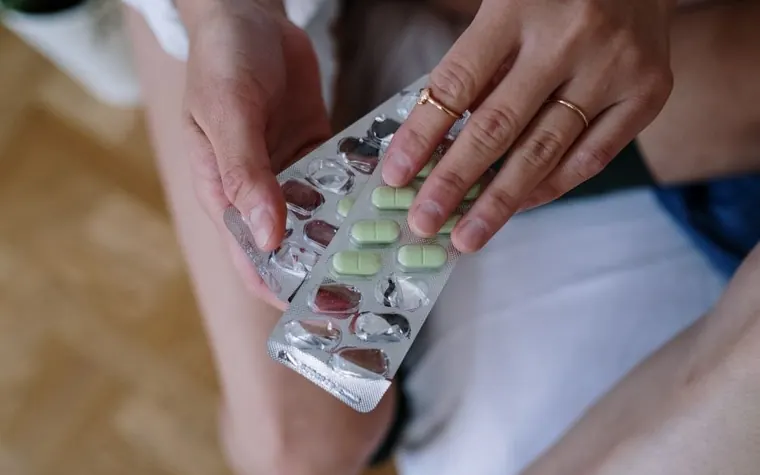 Hands holding a blister pack of green and white tablets over a lap