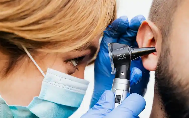 Close-up of a masked clinician examining an ear with an otoscope during an exam