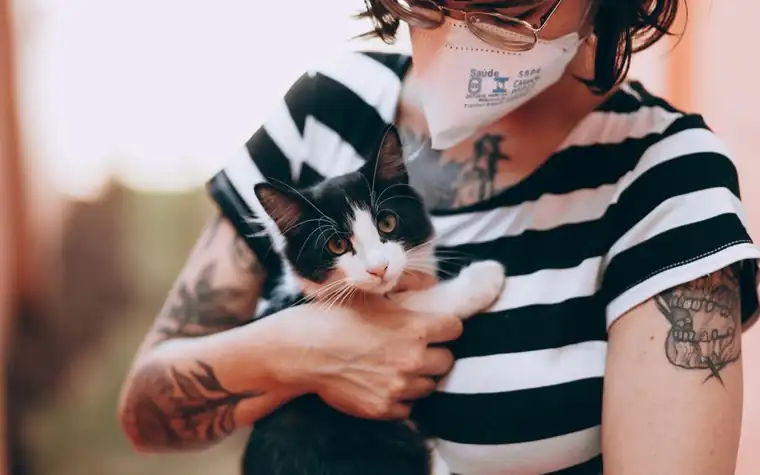 A woman in a face mask holding a black and white cat