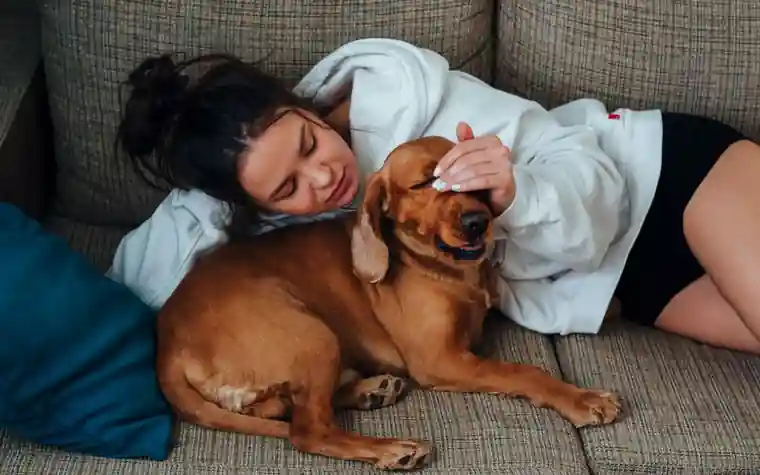 A woman lying on a sofa with a golden dog resting beside her