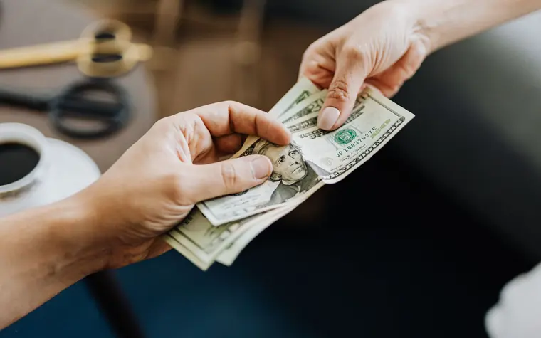 Hands exchanging US dollar bills and coins across a counter