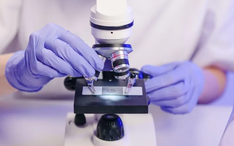 A scientist in gloves adjusting a microscope to examine a slide in a laboratory